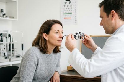 Femme de 40 ans lors d'un bilan visuel chez l'opticien, examinée avec un cadre d'essai ophtalmique par un professionnel en blouse blanche