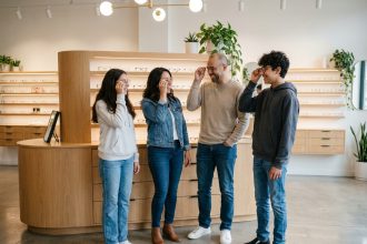 Une famille de quatre personnes essayant des lunettes dans un magasin d'optique moderne, riant ensemble devant les présentoirs de montures